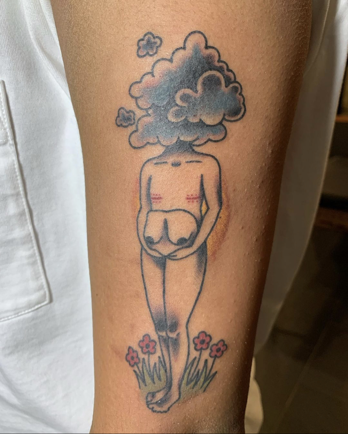 A body with a cloud head and top surgery scars holds their former breasts, while standing on flowers.