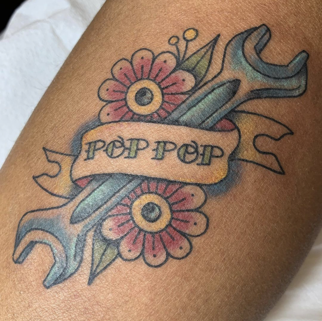 A wrench sits on top of flowers covered by a ribbon that says 'POP POP'.